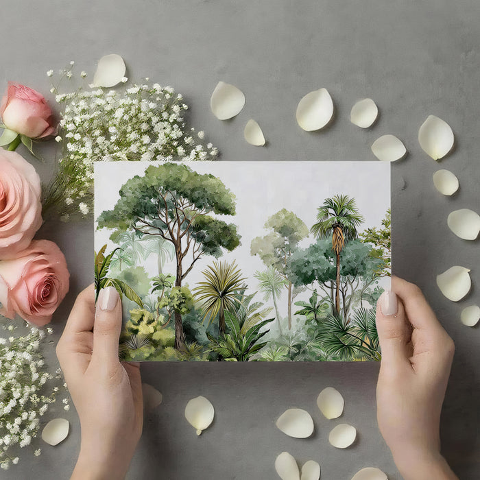 Person holding a card with a forest illustration surrounded by flowers and petals on a gray background