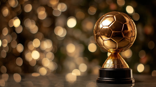 A close-up of a gleaming gold soccer ball trophy against a blurred, golden bokeh light background.