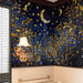 A cozy library room featuring the celestial forest wallpaper as a dark, moody background for dark wood shelving.