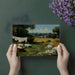 Pastoral oil painting wallpaper featured on a bedroom wall behind a neutral linen headboard