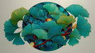 Circular mosaic art featuring teal and turquoise ginkgo leaves with rust-red branches on a cobalt blue background.