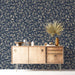 A sophisticated entryway with navy floral wallpaper behind a tufted headboard.
