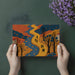 Cozy dining room wall featuring an illustrative village and river scene in warm ochre and navy tones.