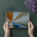 A bright dining room with an impressionist landscape mural, creating a sense of depth behind a minimalist table.