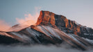 A realistic mountain peak at sunrise with ochre sunlight on rocky cliffs and low mist at the base