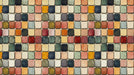 A repeating mural wallpaper pattern of square tiles with a painterly, textured finish in ochre, forest green, and charcoal.