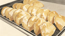A repeating pattern of golden baked empanadas on a dark gray tray in a soft illustrative style