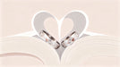 Abstract heart shape formed by folded paper with two wedding rings in soft cream and champagne colors