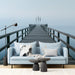 A modern living room featuring a serene misty pier wall mural behind a low profile grey sofa.