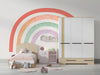 A bright nursery featuring a pastel rainbow arch mural above a wooden crib with neutral textiles.