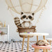A cozy nursery featuring a whimsical raccoon hot air balloon wallpaper behind a white wooden crib and neutral bedding.
