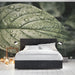 A quiet bedroom with a dark, atmospheric leaf wallpaper that brings a natural, rainy-day feel indoors.