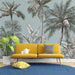 Yellow sofa with decorative pillows in a room with palm tree wallpaper.